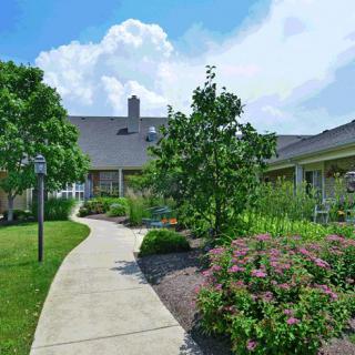 A paved pathway leads through a landscaped garden toward a large building under a sunny sky.