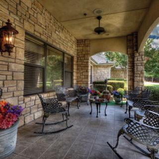 A cozy patio with iron furniture and a stone wall, featuring colorful flowers and a lantern.
