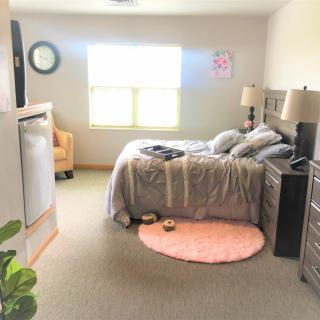 A cozy and well-lit bedroom with a neatly made bed, soft rug, and modern decor.