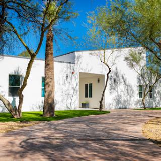 A modern white house surrounded by greenery and bright blue skies.