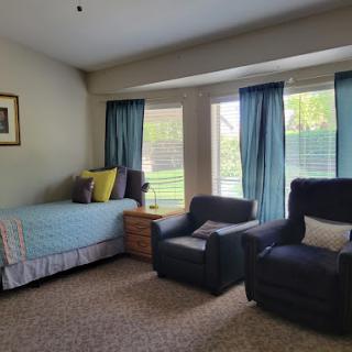 A cozy living space featuring a bed, two comfortable chairs, and large windows that let in plenty of natural light.