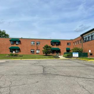 A brick building with green awnings surrounded by a well-maintained lawn and a clear sky.