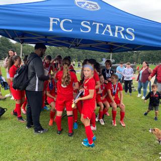 A spirited group of young athletes from FC Stars gather under their team tent, ready for action.
