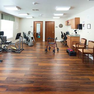 A well-equipped rehabilitation center with various exercise equipment and a wooden floor.