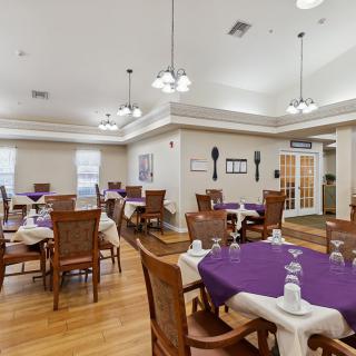 A well-lit dining room with neatly arranged tables and chairs, featuring a wooden floor and elegant lighting.