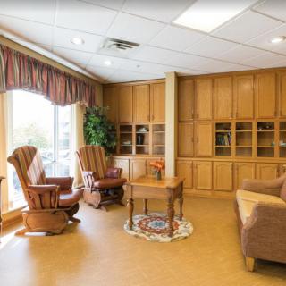 A cozy living room with rocking chairs, wooden shelves, and sunlight streaming through large windows.