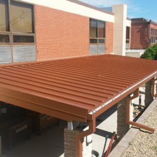 A newly constructed metal roof over a patio area adjacent to a building.