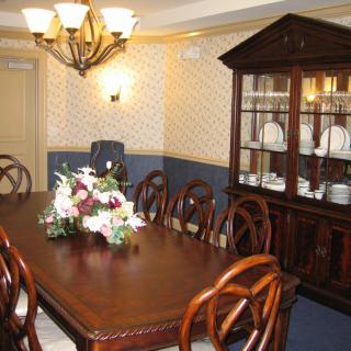 A dining room with a wooden table, chairs, and a cabinet, elegantly decorated with a floral centerpiece and chandelier.