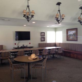 A cozy dining area with tables, chairs, chandeliers, and a hat on a table.