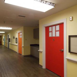 A well-lit hallway with brightly colored doors and framed pictures on the walls.