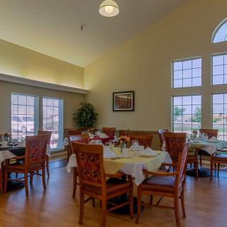 A well-lit dining area with neatly arranged tables and chairs, featuring large windows and elegant decor.