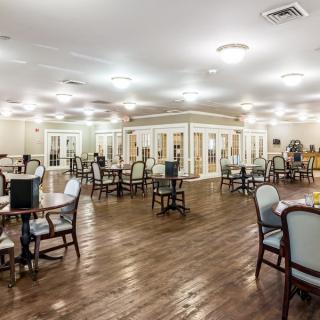 A spacious dining area with wooden floors, tables, and chairs, lit by ceiling lights.