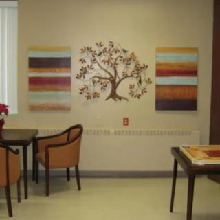 An indoor seating area with tables and chairs, featuring wall art including a tree design and colorful panels.