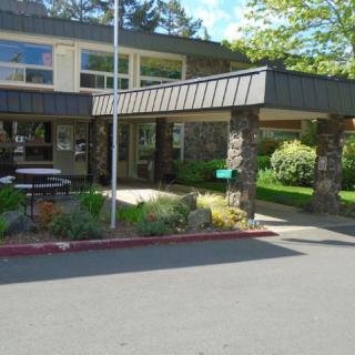 Exterior view of a building entrance with landscaping and a flagpole on a sunny day.