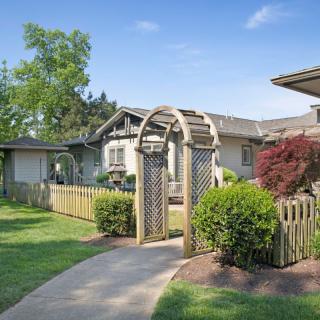 A charming house with a garden, featuring a pathway leading through an archway surrounded by greenery.