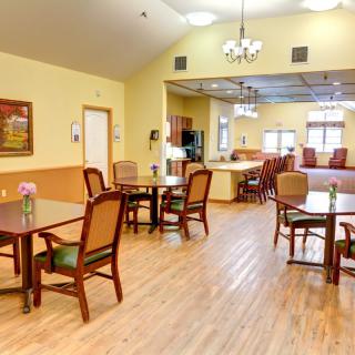 A spacious dining room with wooden flooring and neatly arranged tables and chairs under ceiling lights.