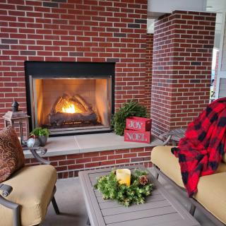 A cozy outdoor seating area with a brick fireplace, comfortable chairs, and a warm blanket.