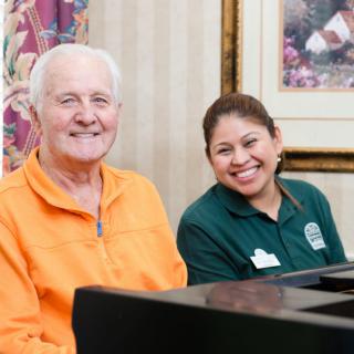 Two people sitting and smiling indoors near a piano.