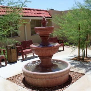 A three-tiered fountain in an outdoor garden patio with surrounding benches and trees.