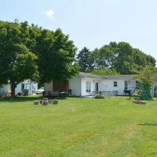 A rural house with a large grassy yard and surrounding trees.