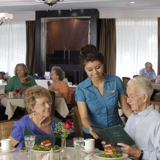 A waitress serves a meal to senior patrons at a restaurant.