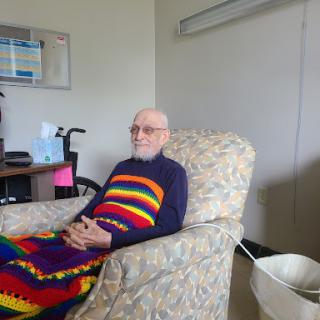 An elderly man relaxing in a cozy chair, wrapped in a colorful blanket.