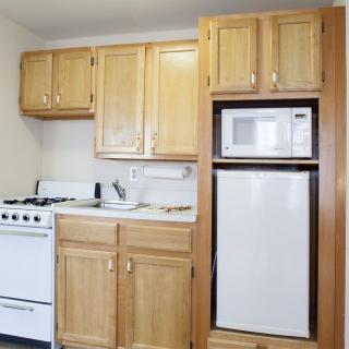 A compact kitchen with wooden cabinets, a stove, microwave, and refrigerator.
