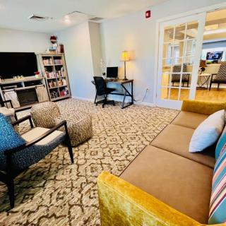 A cozy living room with a sofa, chairs, a television, and a bookshelf, featuring a work desk in the corner.