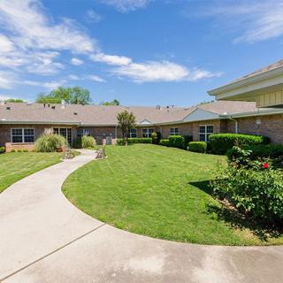 A view of a building with a well-maintained garden and pathway under a blue sky.