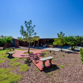 A landscaped garden with benches, trees, and a paved pathway under a clear blue sky.