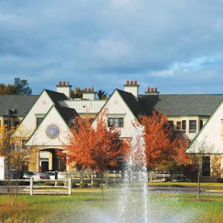 A scenic view of a building surrounded by autumn foliage and a fountain under a blue sky.