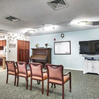A cozy room with chairs facing a piano and a television, providing a space for gatherings or entertainment.