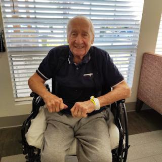 An elderly man with a warm smile sitting in a wheelchair indoors.