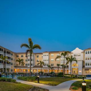 A well-lit residential building with palm trees at night.
