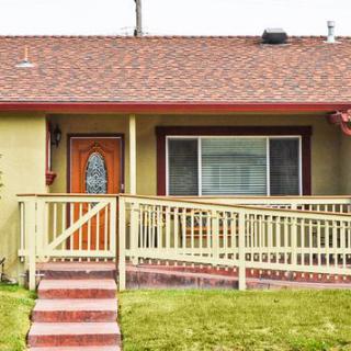 A house with a ramp leading to the front door, featuring a large window and a red roof.