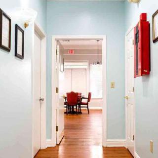 A bright office hallway with light blue walls leading to a meeting room with red chairs.