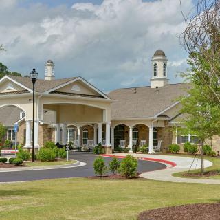 A well-maintained building with a landscaped garden and driveway under a cloudy sky.
