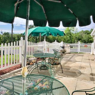 A sunny patio with green umbrellas and metal furniture, surrounded by a white picket fence.