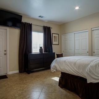 A modern bedroom featuring a neatly made bed, wall-mounted television, and large windows with dark curtains.