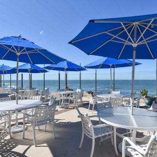 An outdoor beachside restaurant with blue umbrellas and ocean views on a sunny day.