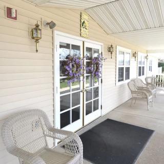 A welcoming porch with wicker chairs and decorative wreaths on double doors.