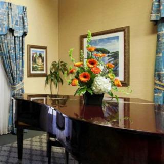 A beautifully decorated room featuring a grand piano with a floral arrangement on top, surrounded by artwork and elegant curtains.