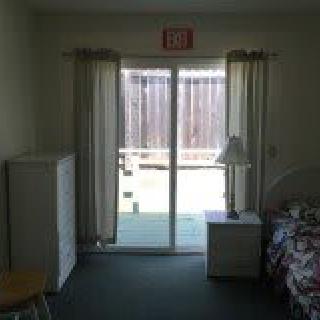 A simple room with a bed, nightstand, and patio door leading outside.