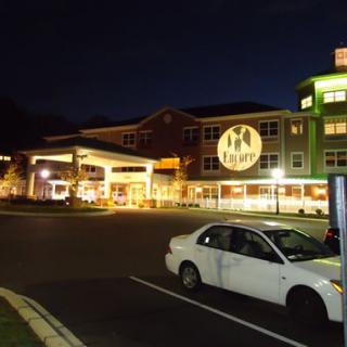 A nighttime view of a building with a light projection on its wall, next to a parked car in a parking lot.