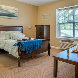 A cozy bedroom interior with a bed, dresser, and large window.