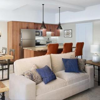 A modern open-concept living space featuring a cozy sofa with decorative pillows, adjacent to a kitchen area with pendant lighting and wooden cabinetry.