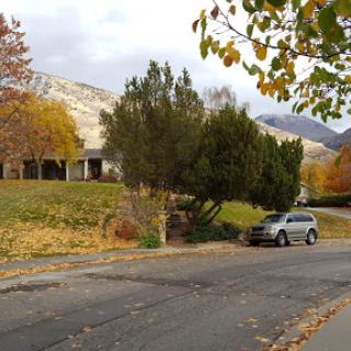 A serene autumn scene featuring a house surrounded by colorful trees and mountains in the background.