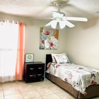 A cozy bedroom featuring natural light, a ceiling fan, and floral artwork.