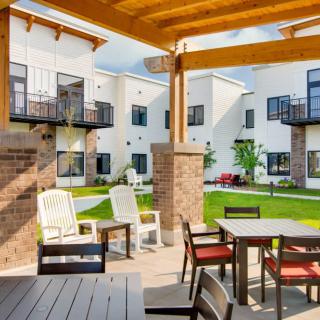 A modern apartment complex with an inviting outdoor patio area featuring tables and chairs in a landscaped courtyard.
