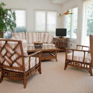 A cozy living room with rattan furniture, a television, and large windows.